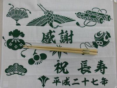 鶴や松など長寿のシンボルが描かれた手ぬぐいを広げた上に置かれた長寿祝箸の写真