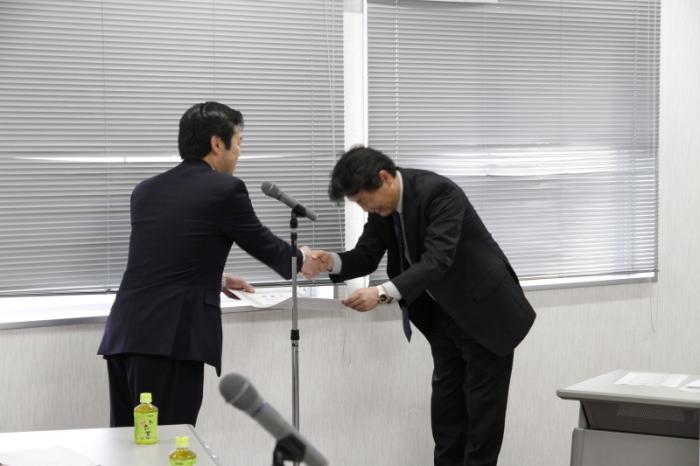 会議室にて辻市長から感謝状を受けとりつつ市長と握手する協会代表の写真