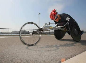マラソン競技用車椅子に乗って屋外の道路を走る、西田さんの練習風景の写真