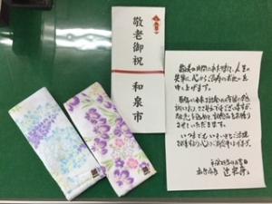 敬老祝品の手拭ガーゼと市長からの添え状、熨斗紙を並べた写真