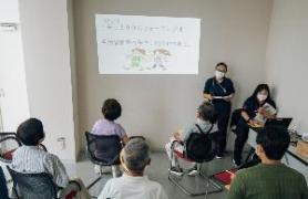 地域包括支援センターコーナーで、プロジェクターを使っての講話を聴講している市民の写真