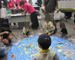 食のコーナーで魚釣りゲームのルールを利用した食品つりに参加する子供たちの写真