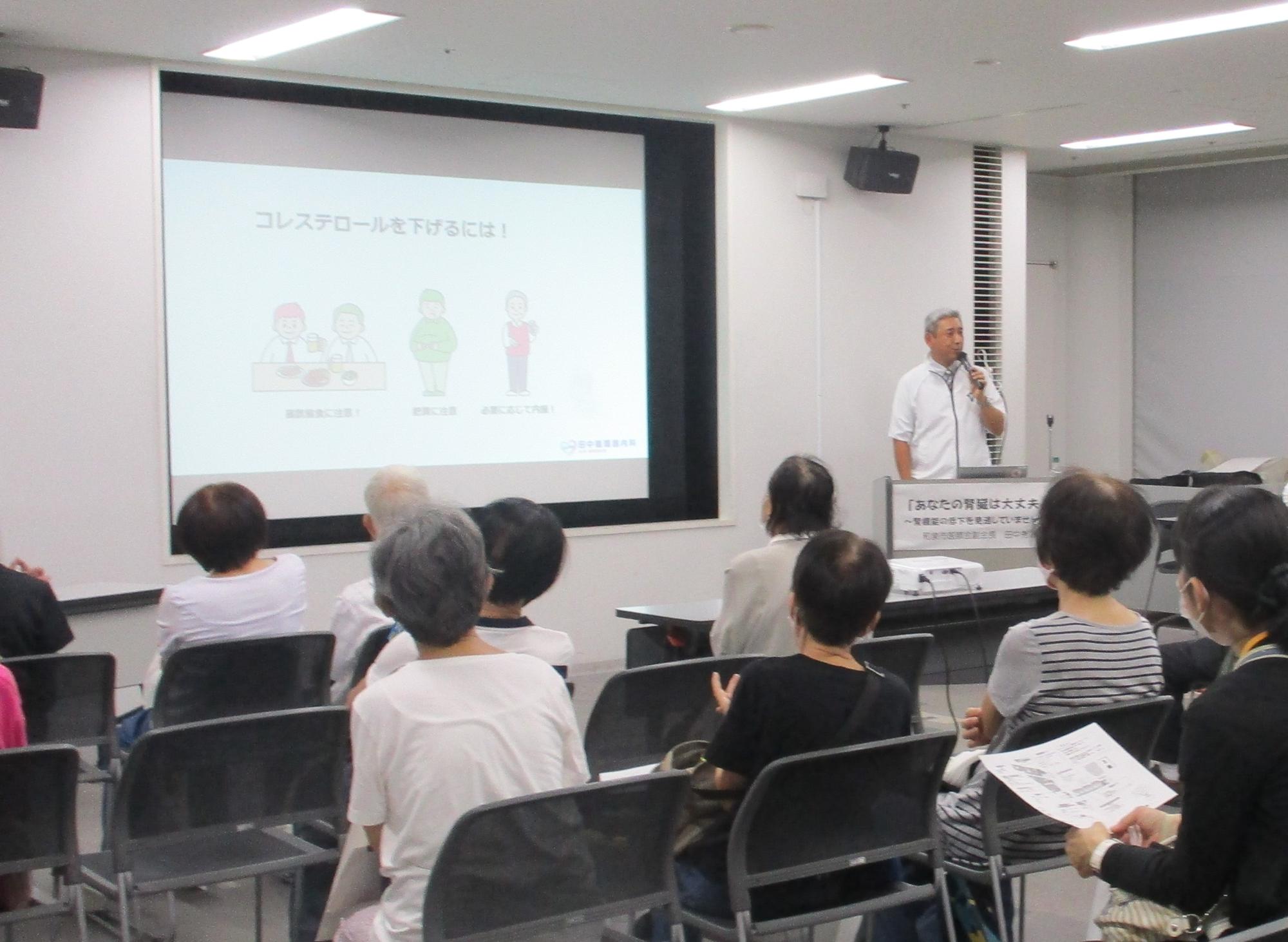 講演会にてプロジェクターを使っての講演を聴講する来場者たちの写真