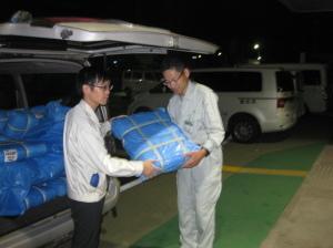 和泉市の職員が総社市の職員に支援物資のブルーシートを手渡ししている写真