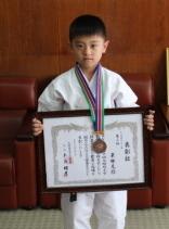 メダルを首にかけ、賞状を掲げる栗林克弥さんの写真