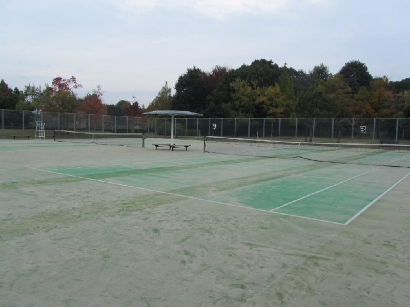 屋根付きのベンチ2基を挟んで2面分を設置したテニスコートの写真